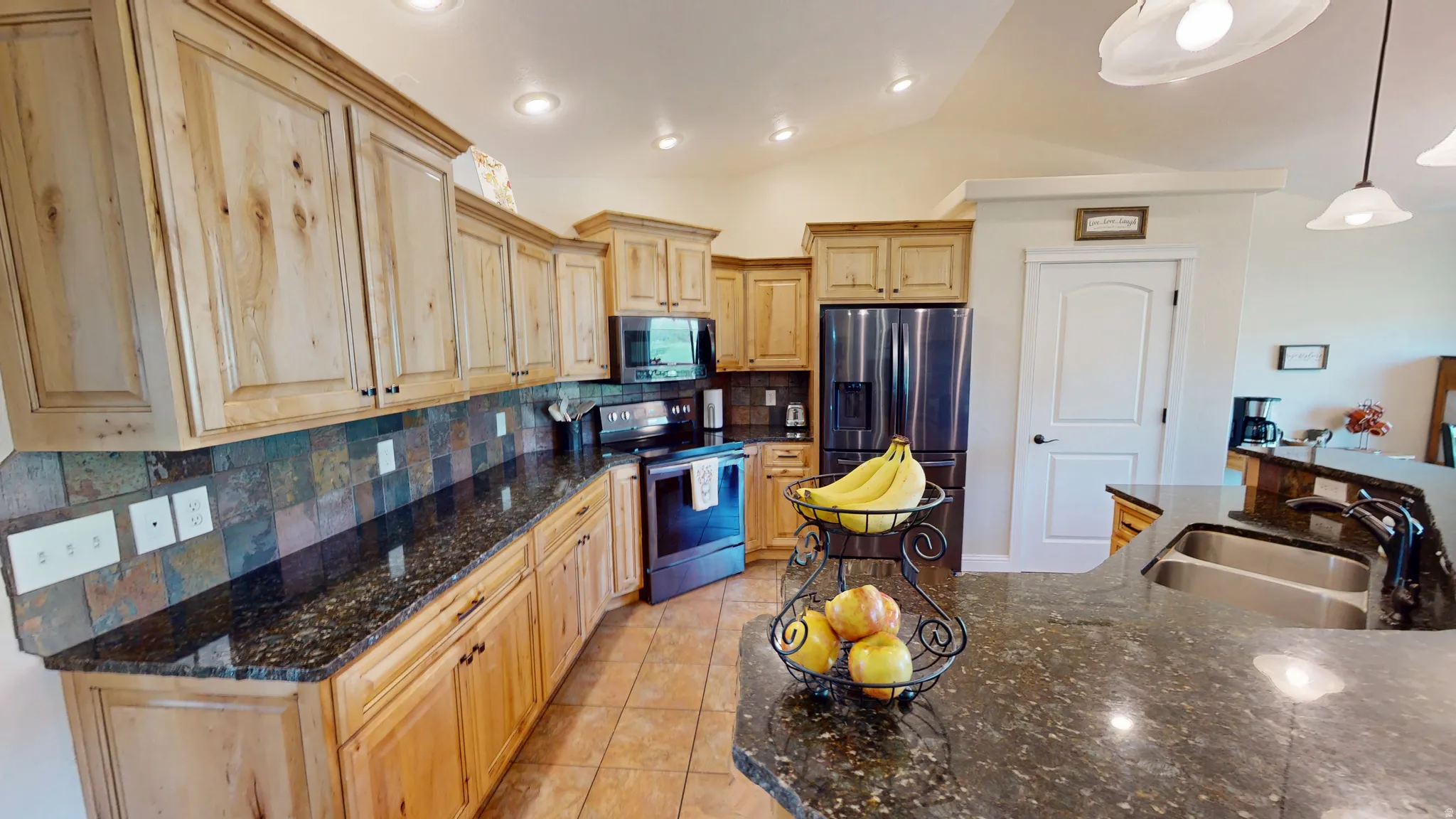 Kitchen with decorative backsplash, stainless steel appliances, vaulted ceiling, dark stone counters, and light wood finish cabinetry