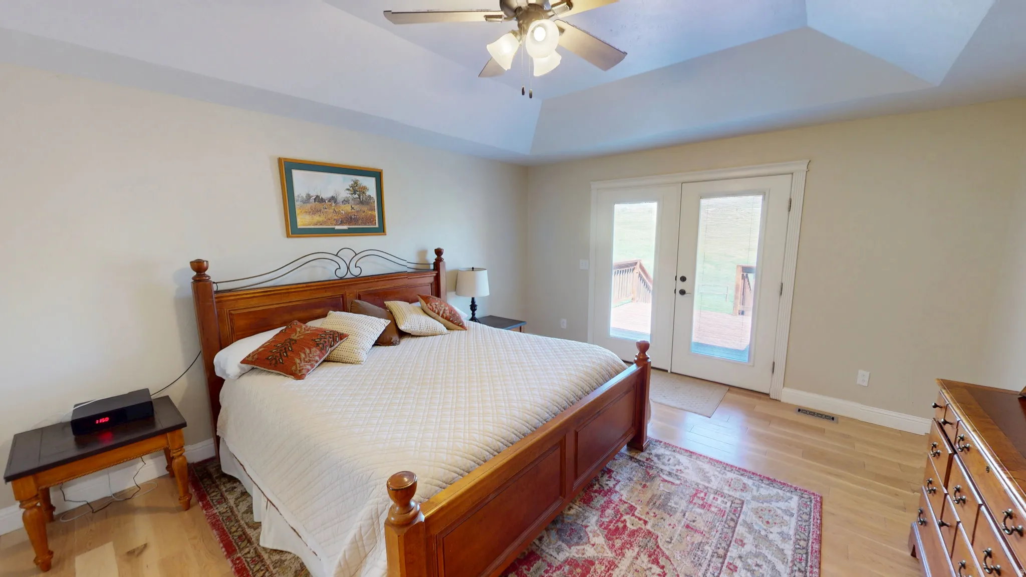 Bedroom featuring a raised ceiling, light wood-style flooring, access to exterior, french doors, and a ceiling fan