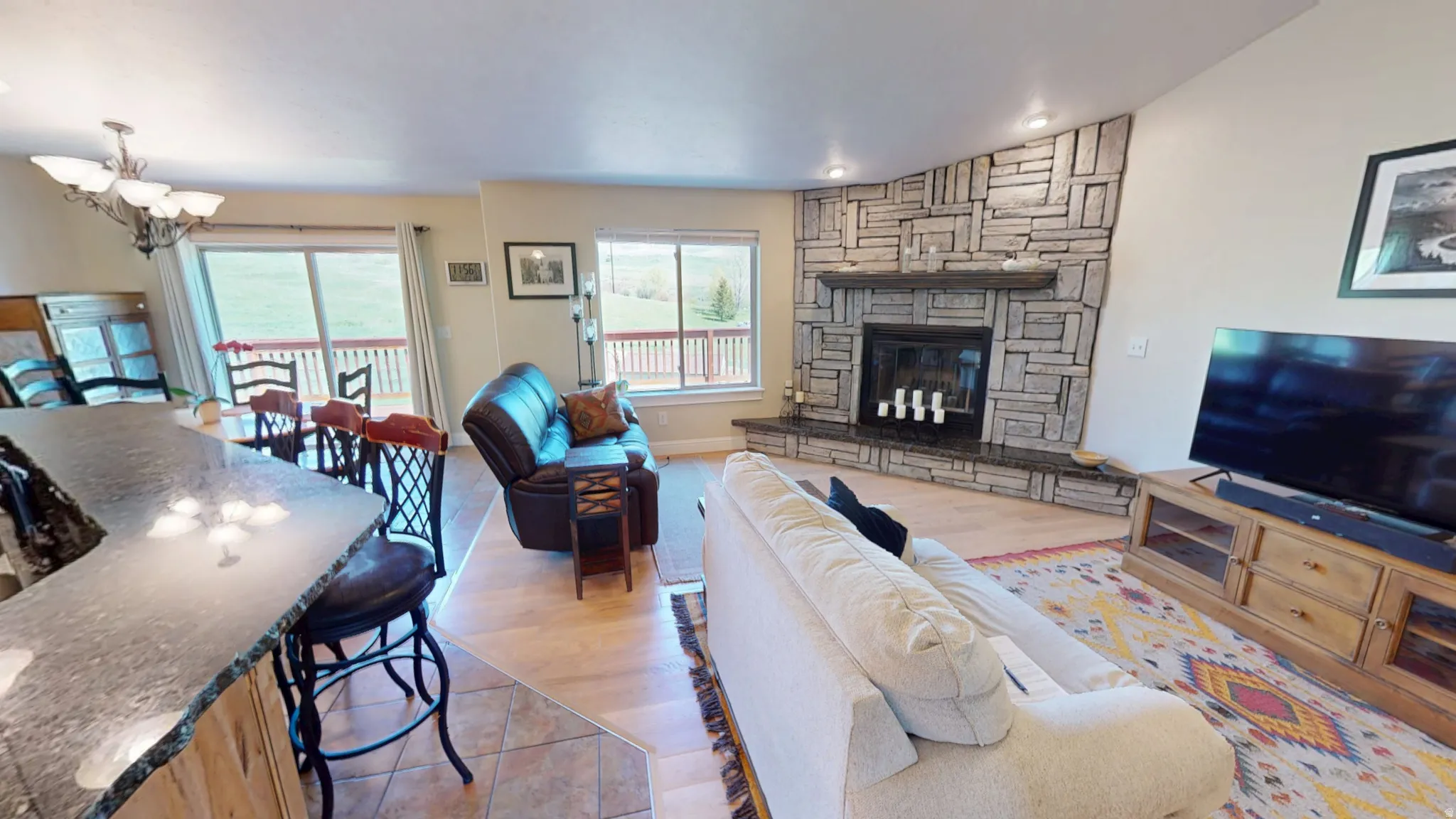 Living area with a stone fireplace, lofted ceiling, light wood-type flooring, and a chandelier