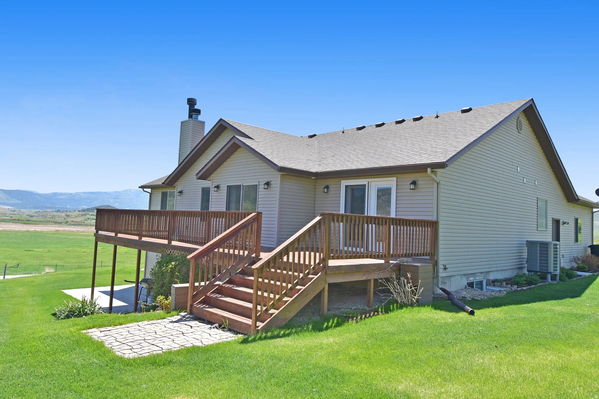 Back of house featuring a lawn, a deck with mountain view, roof with shingles, a chimney, and a patio area