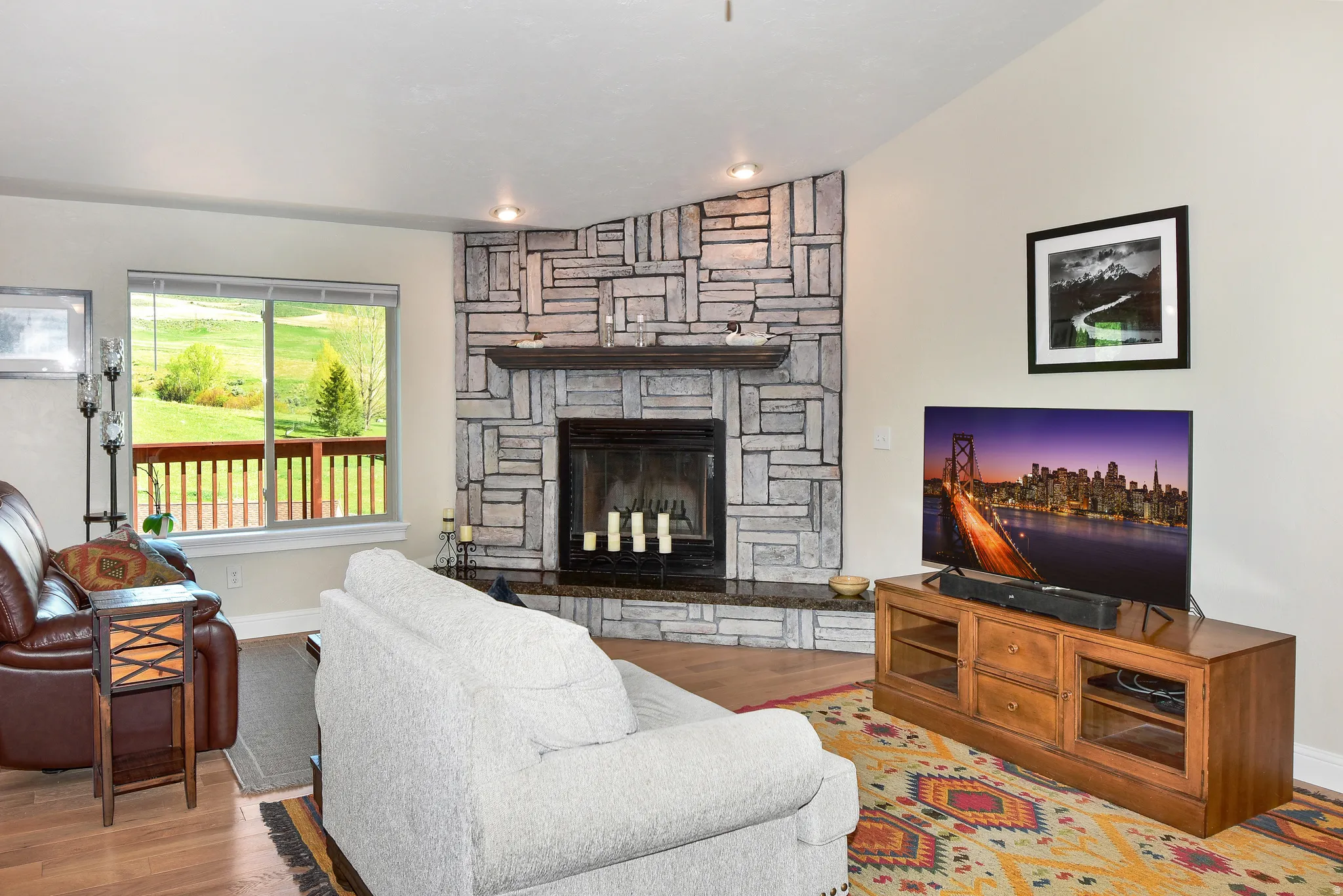 Living room featuring wood finished floors, a stone fireplace, and vaulted ceiling