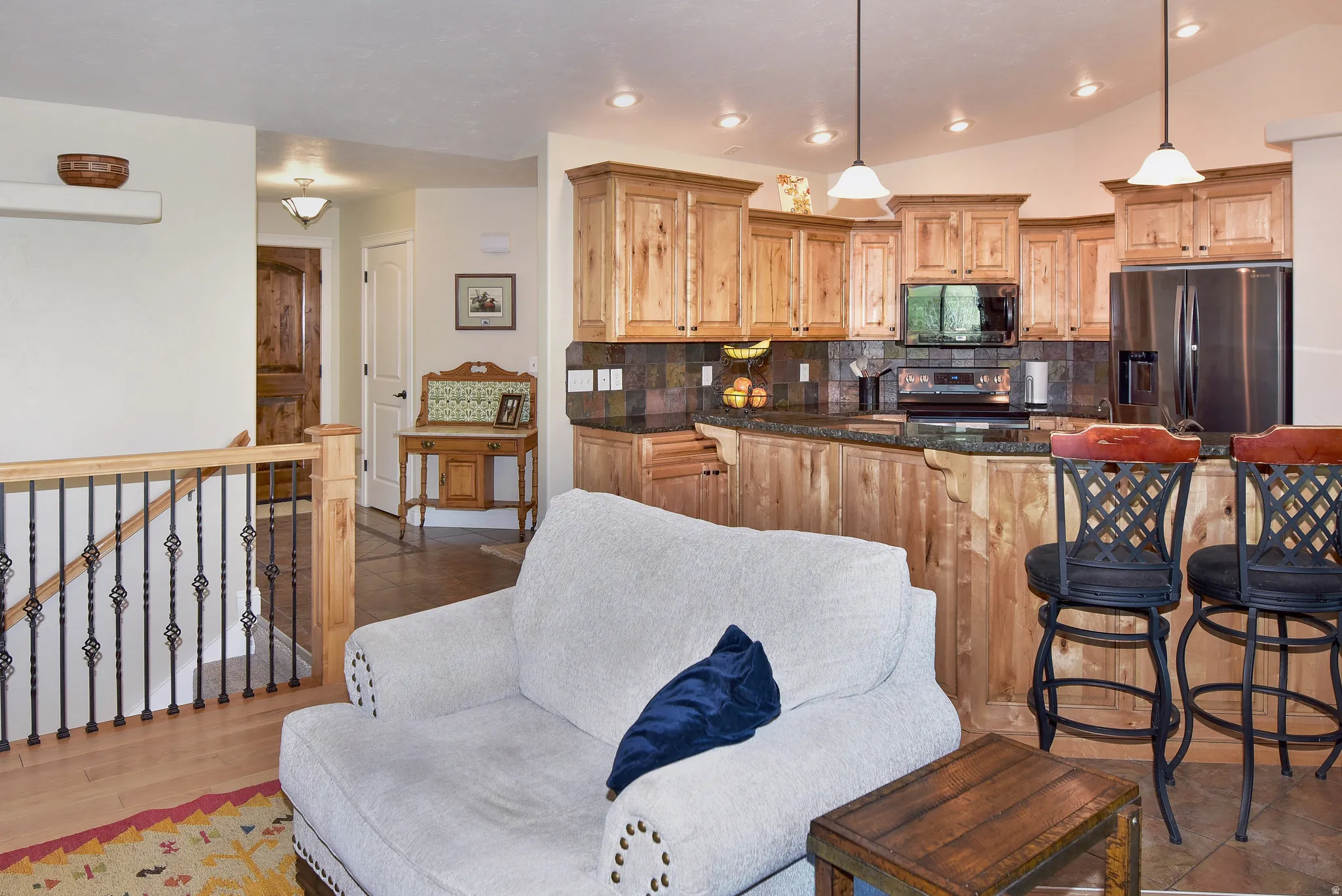 Kitchen with backsplash, stainless steel appliances, vaulted ceiling, light wood finish cabinetry, and dark stone counters