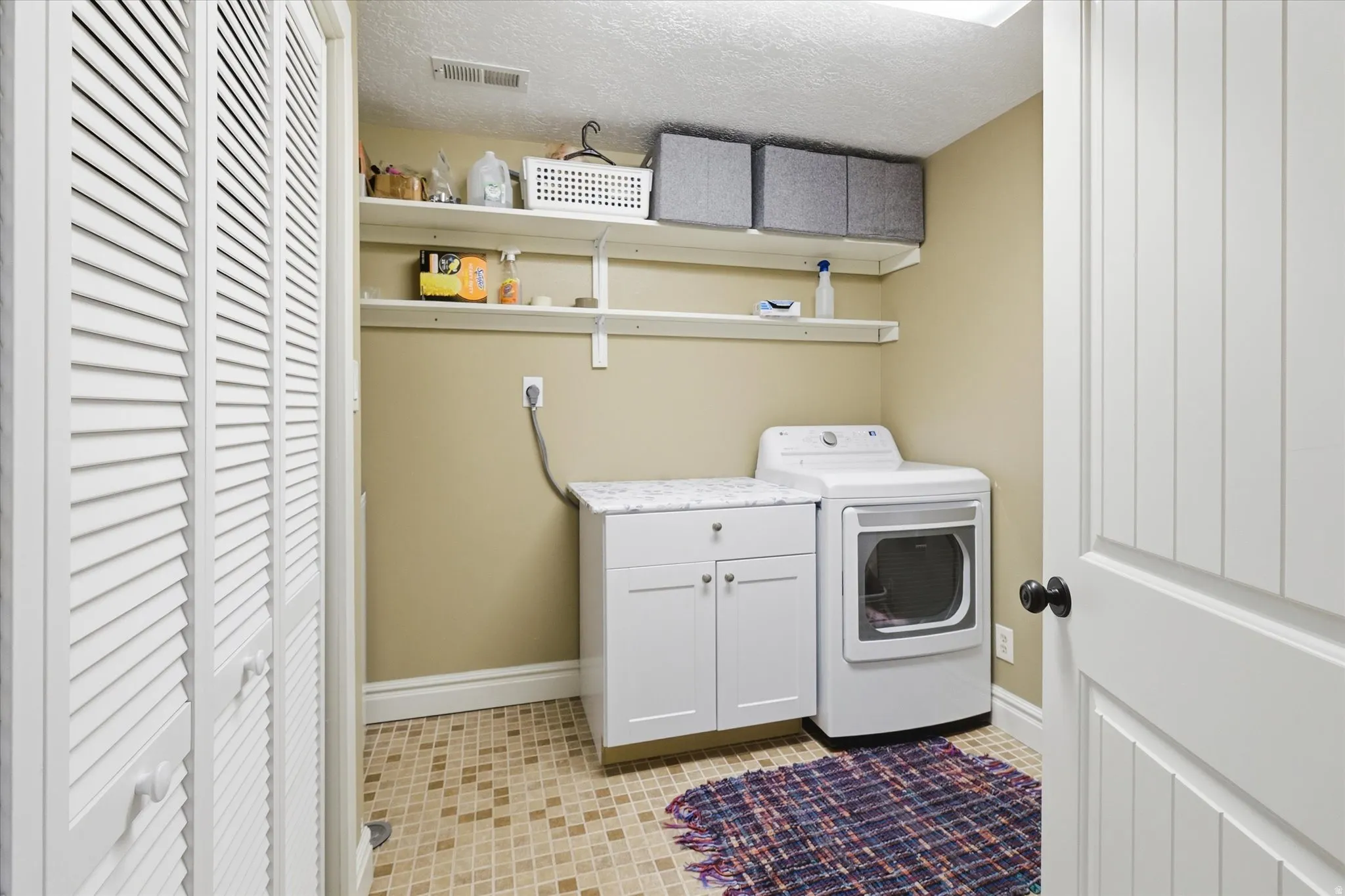 Laundry room featuring a textured ceiling, light tile patterned flooring, and cabinet space