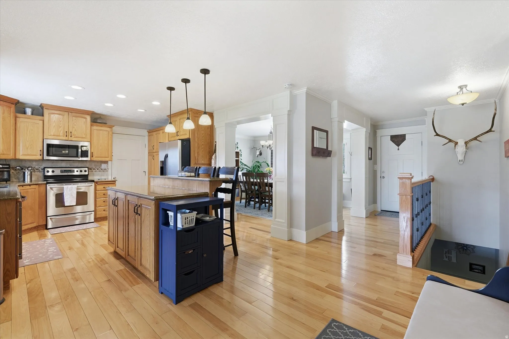 Kitchen featuring stainless steel appliances, a kitchen bar, light wood-style floors, decorative columns, and a center island