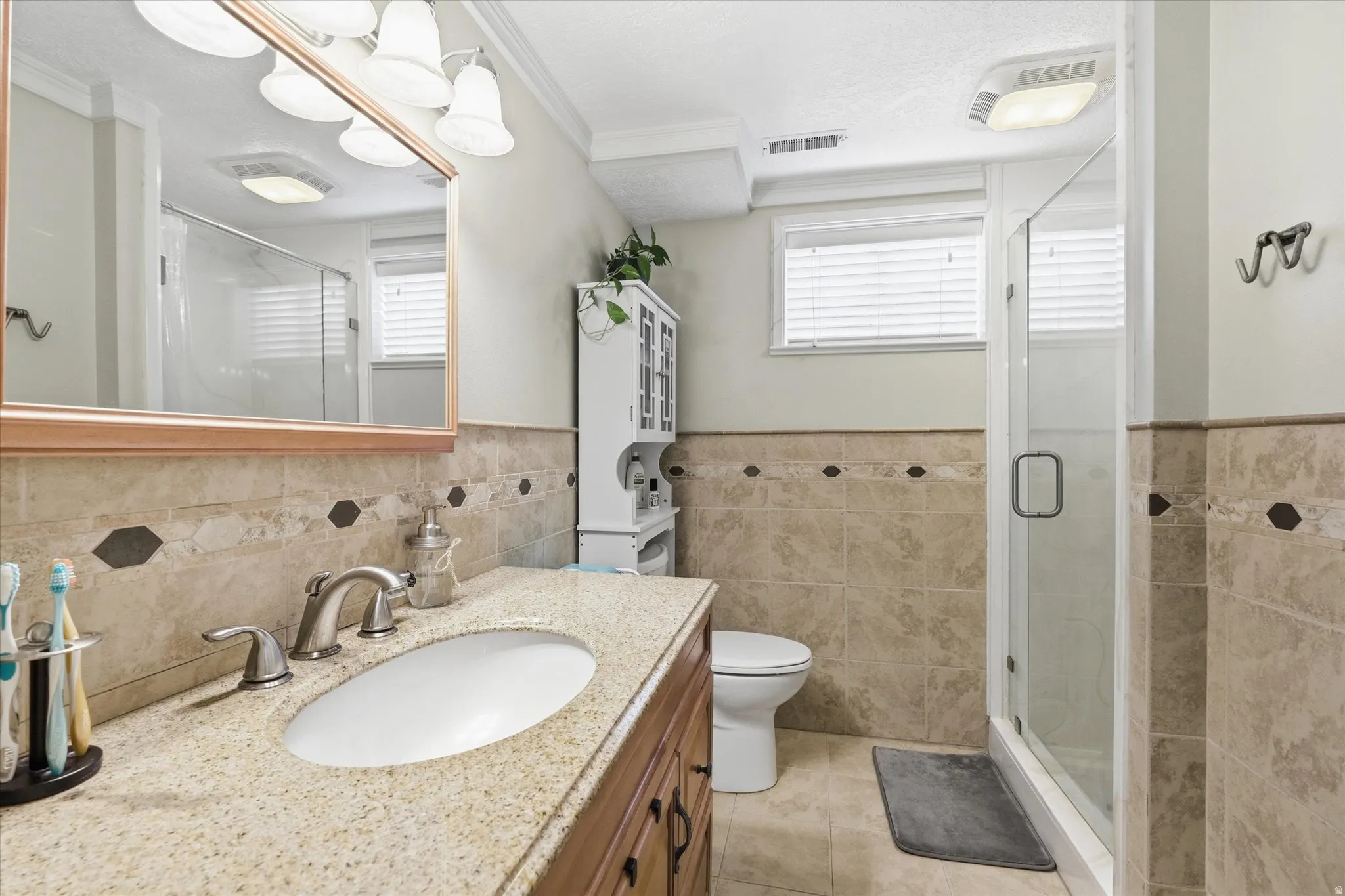 Full bath featuring vanity, a stall shower, wainscoting, healthy amount of natural light, and tile walls