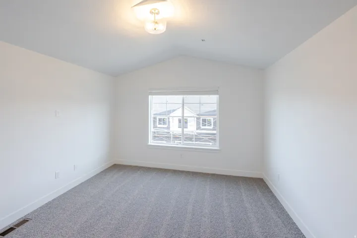 Vaulted ceiling with an attached light fixture, a large window, and gray carpeting
