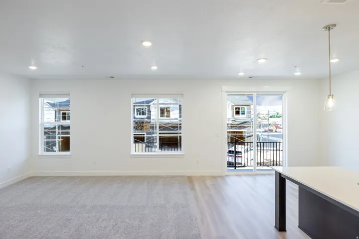 Recessed ceiling lighting, multiple windows, sliding glass door, wood-finish flooring, and a kitchen island with a light-toned countertop