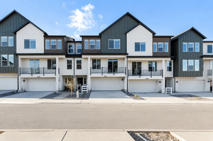 Modern townhome exterior featuring white stucco, dark vertical siding, multiple balconies with black railings, and attached garages