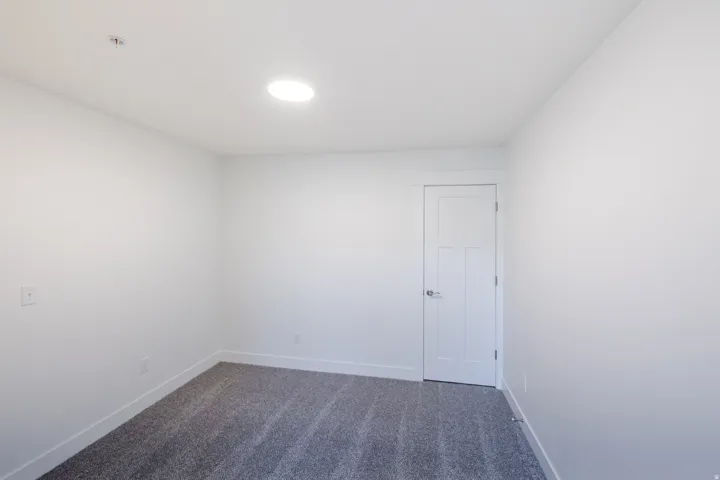 Recessed ceiling lighting, white interior door, light gray walls, and gray patterned carpeting
