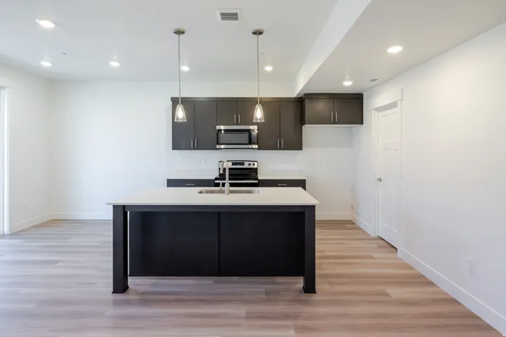 Kitchen island with a light-toned countertop and integrated sink, stainless steel appliances, dark wood-finish cabinetry, recessed lighting, and wood-finish flooring