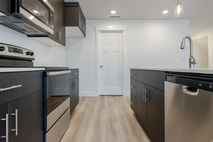 Modern kitchen featuring dark wood-finish cabinetry, stainless steel appliances, light-toned countertops, and wood-finish flooring