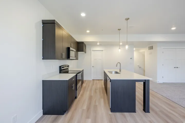 Kitchen with dark wood-finish cabinetry, light countertops, stainless steel appliances, and a central island with a sink
