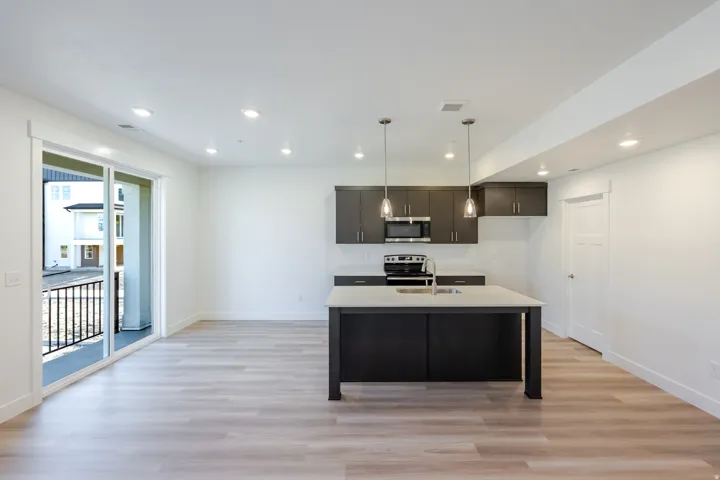 Open-concept living space with wood-finish flooring, recessed lighting, and a sliding glass door to a balcony