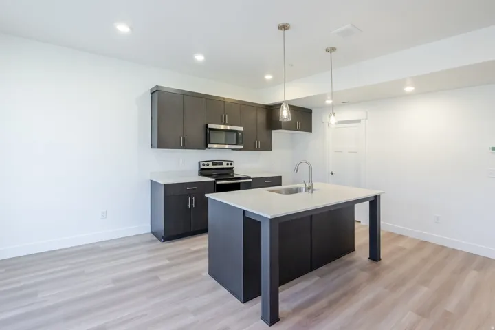 Contemporary kitchen featuring dark wood-finish cabinetry, stainless steel appliances, a center island with sink, and pendant lighting