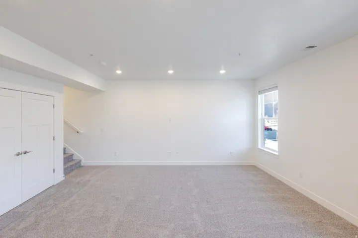 Recessed lighting, light-colored carpeting, white walls, white trim, and a window with white casing