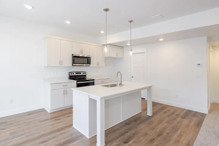 Kitchen featuring an island with an undermount sink, stainless steel appliances, white cabinetry, recessed lighting, and wood-finish flooring