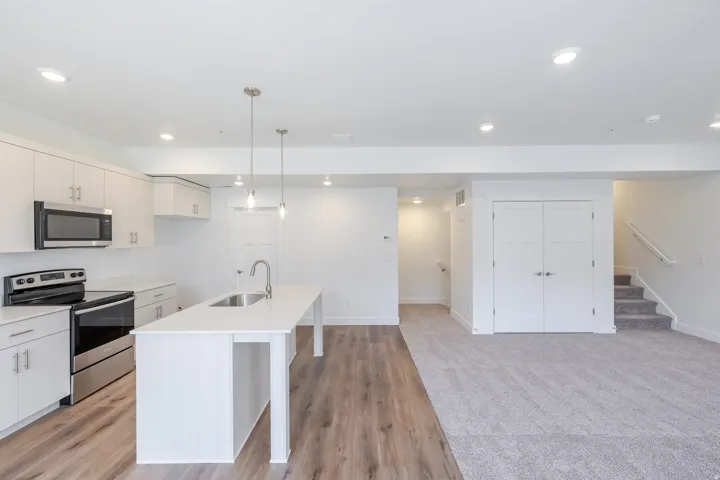 Modern kitchen featuring stainless steel appliances, white cabinetry, a kitchen island with sink, pendant lighting, and wood-finish flooring