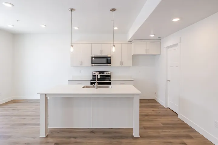 Kitchen featuring a center island with integrated sink, stainless steel appliances, pendant lighting, and wood-finish flooring