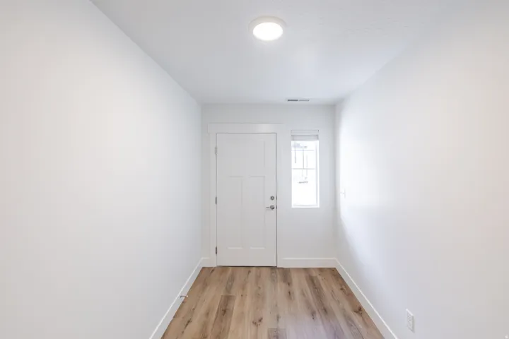 Entryway featuring wood-finish flooring, a contemporary flush-mount ceiling light, a white paneled door, and a single pane window with blinds