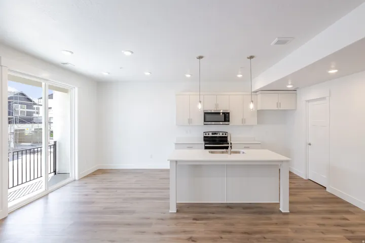 White kitchen featuring an island with an undermount sink, stainless steel appliances, pendant lighting, and wood-finish flooring