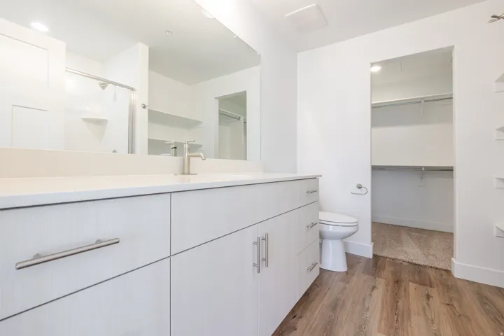 White vanity with brushed nickel hardware, light-toned countertop, and wood-finish flooring