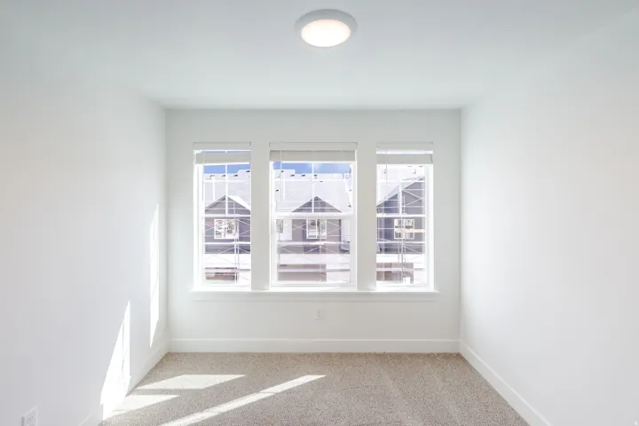 Triple window assembly with blinds, flush-mount ceiling light, and neutral carpet