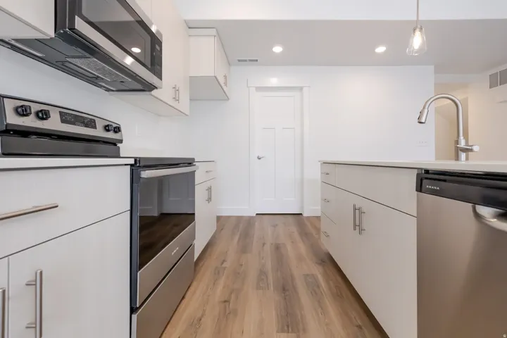 White cabinetry, wood-finish flooring, stainless steel appliances, recessed lighting, and a kitchen island with a built-in sink