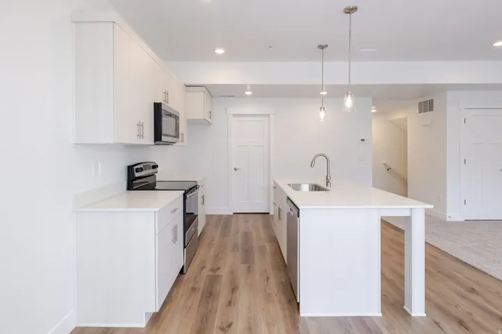 Kitchen featuring white cabinetry, stainless steel appliances, a center island with a sink, pendant lighting, and wood-finish flooring