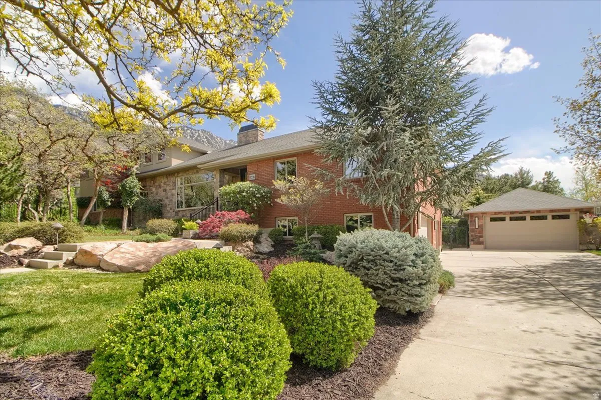 View of front of house featuring brick siding, a chimney, an outdoor structure, and a garage