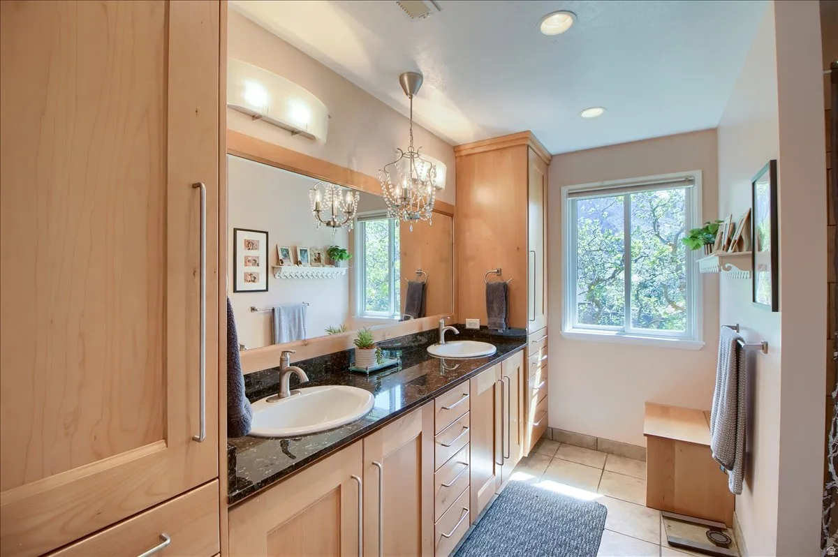 Ensuite bathroom featuring double vanity, suspended lighting, and light tile patterned flooring
