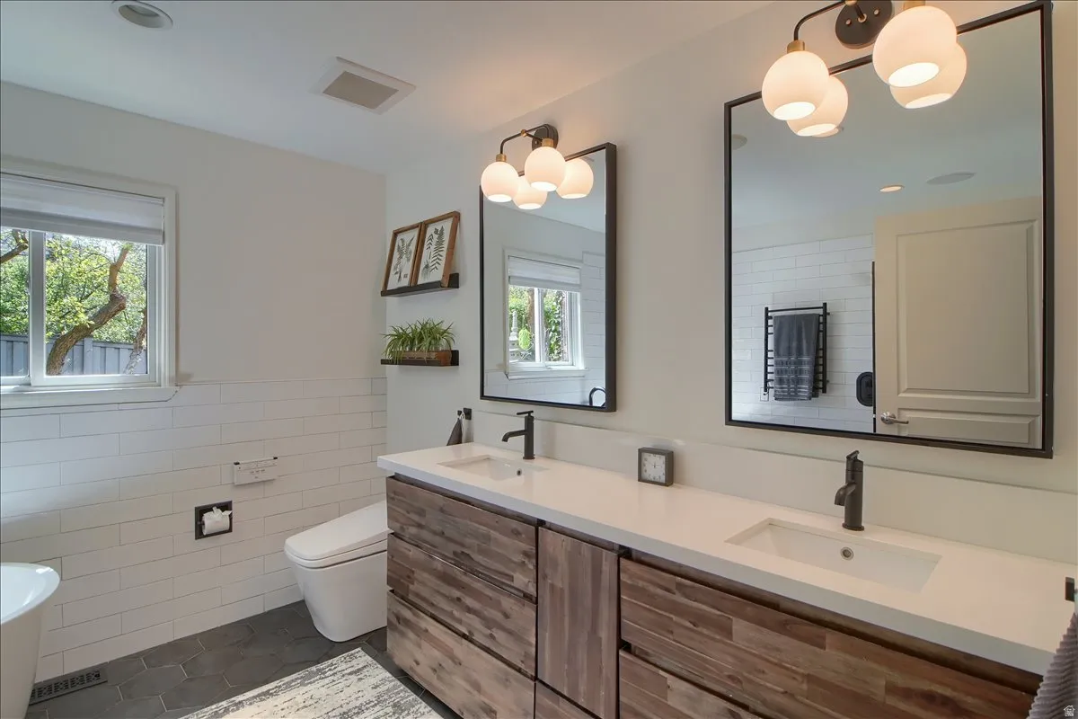 Master bath with double vanity, suspended lighting, tile walls, a wainscoted wall, and dark tile patterned flooring