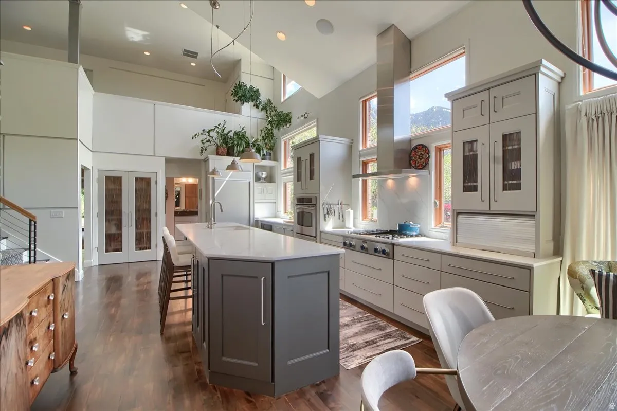 Kitchen with a high ceiling, a breakfast bar area, french doors, a large island with sink, and dark wood-style flooring