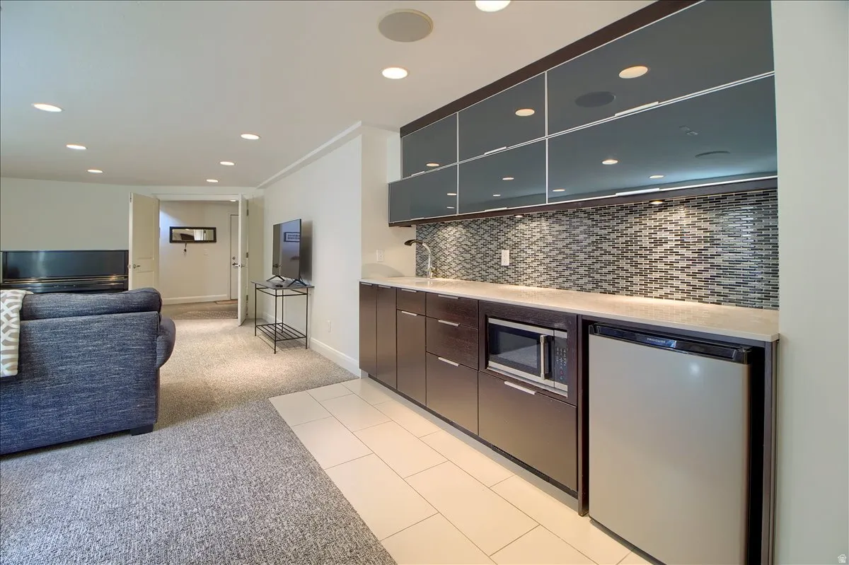 Two tone basement kitchen featuring open floor plan, refrigerator, recessed lighting, light colored carpet, and stainless steel microwave
