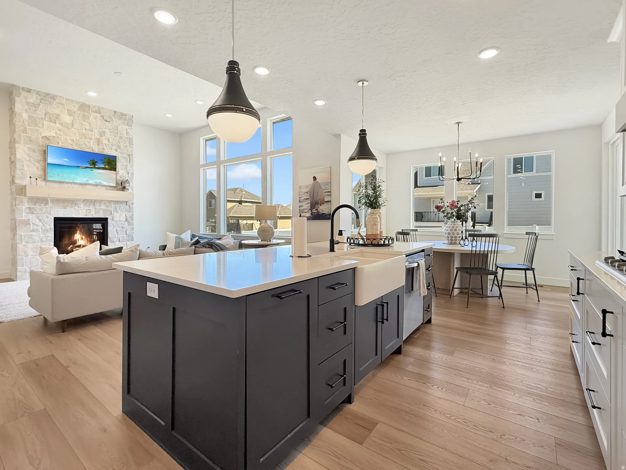 Kitchen featuring a fireplace, open floor plan, an island with sink, light wood-style flooring, and a textured ceiling