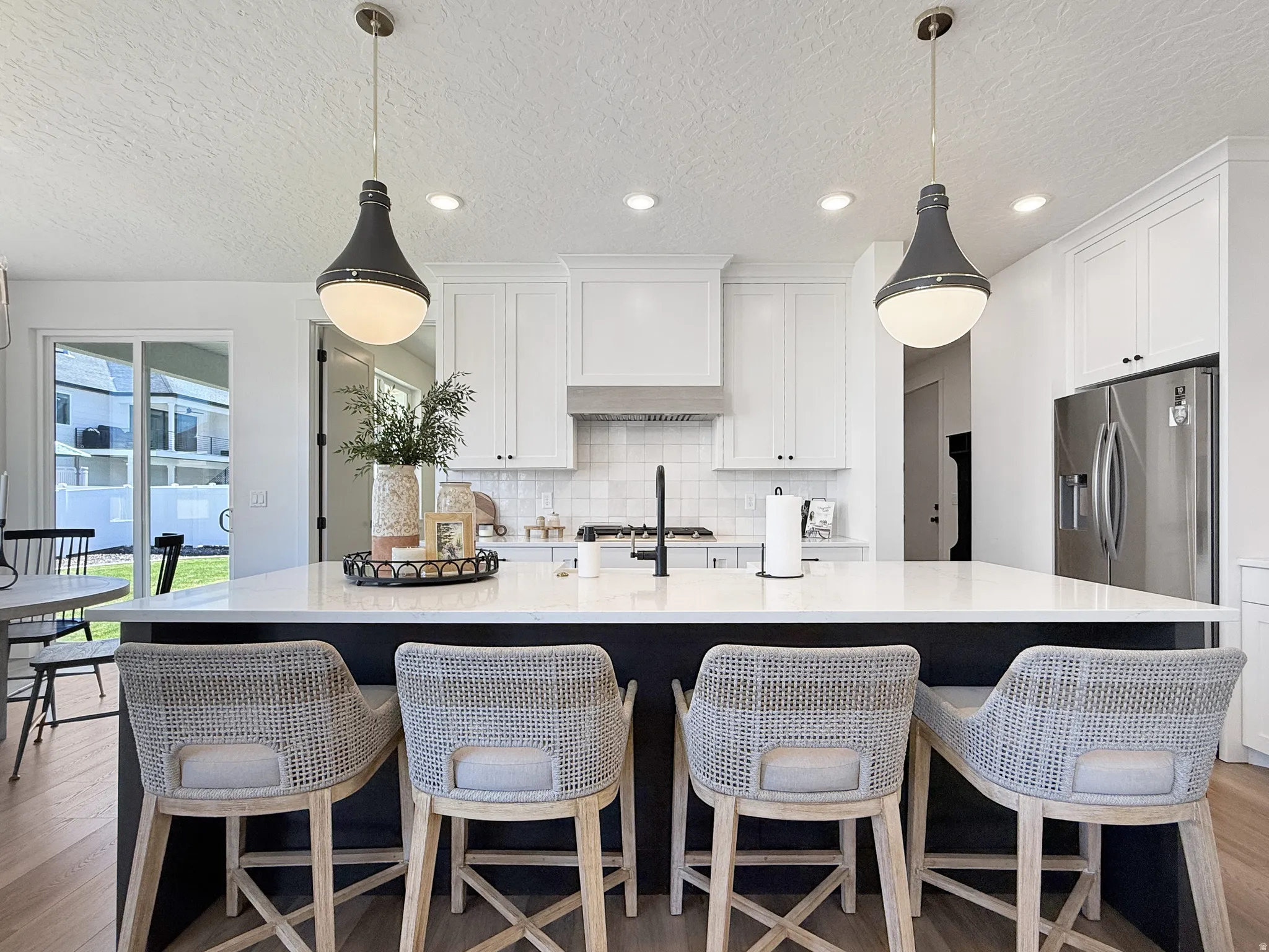 Kitchen featuring a spacious island, light wood-type flooring, a textured ceiling, light stone countertops, and a kitchen breakfast bar