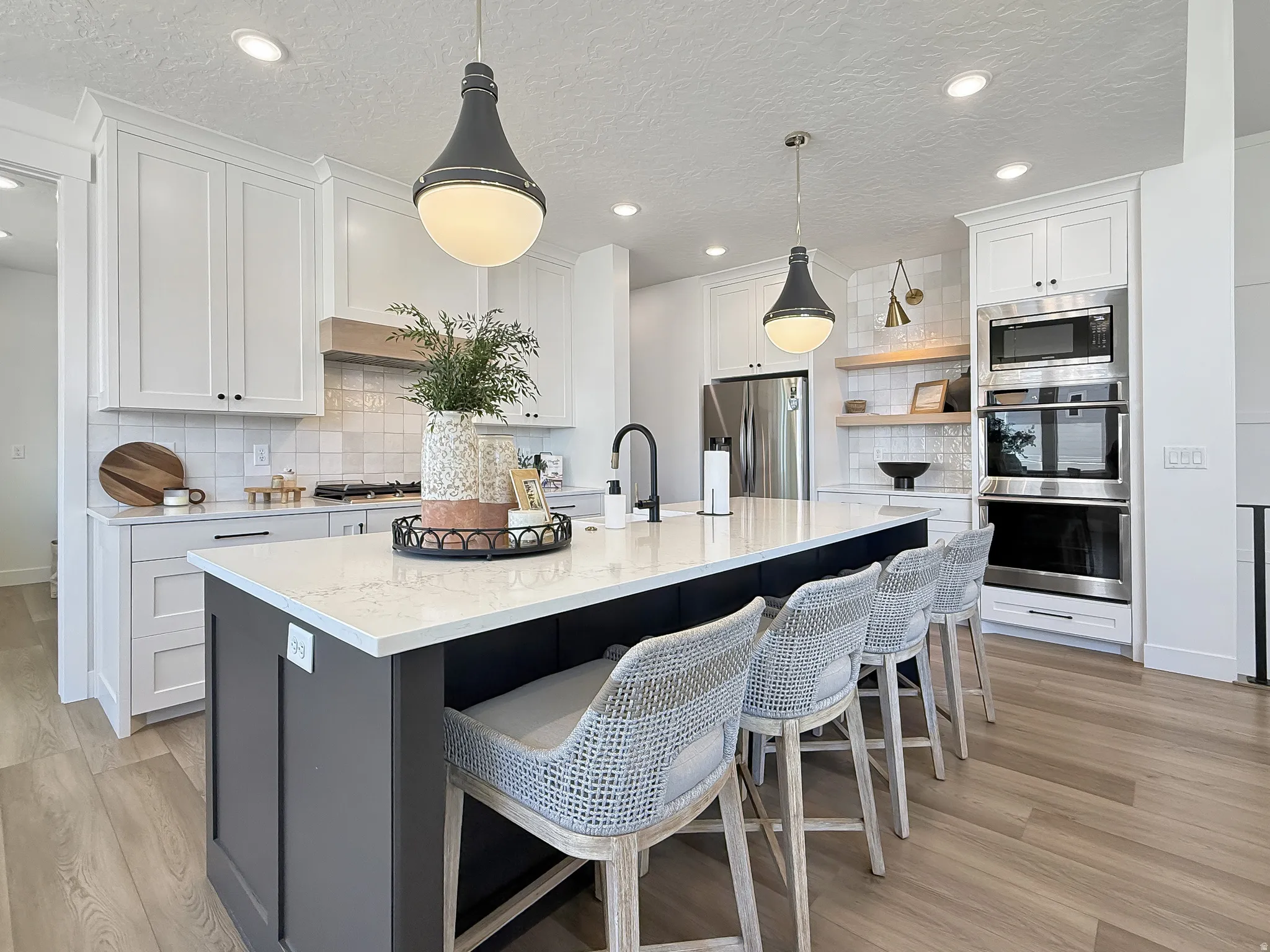 Dual tone kitchen with two tone cabinetry, tasteful backsplash, stainless steel appliances, a kitchen island with sink, and hanging light fixtures