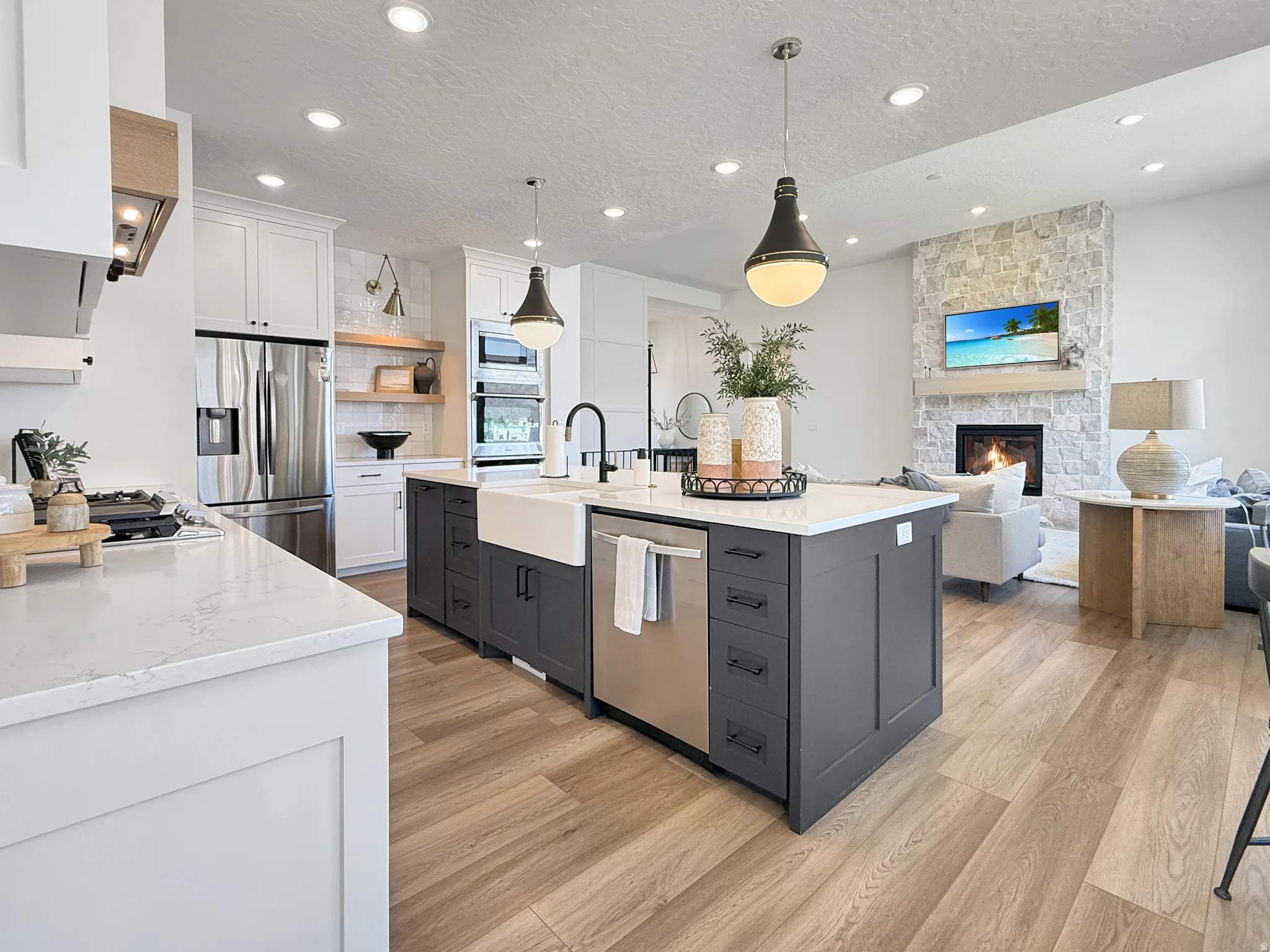 Dual tone kitchen featuring two tone color scheme, a textured ceiling, open floor plan, stainless steel appliances, and light stone counters
