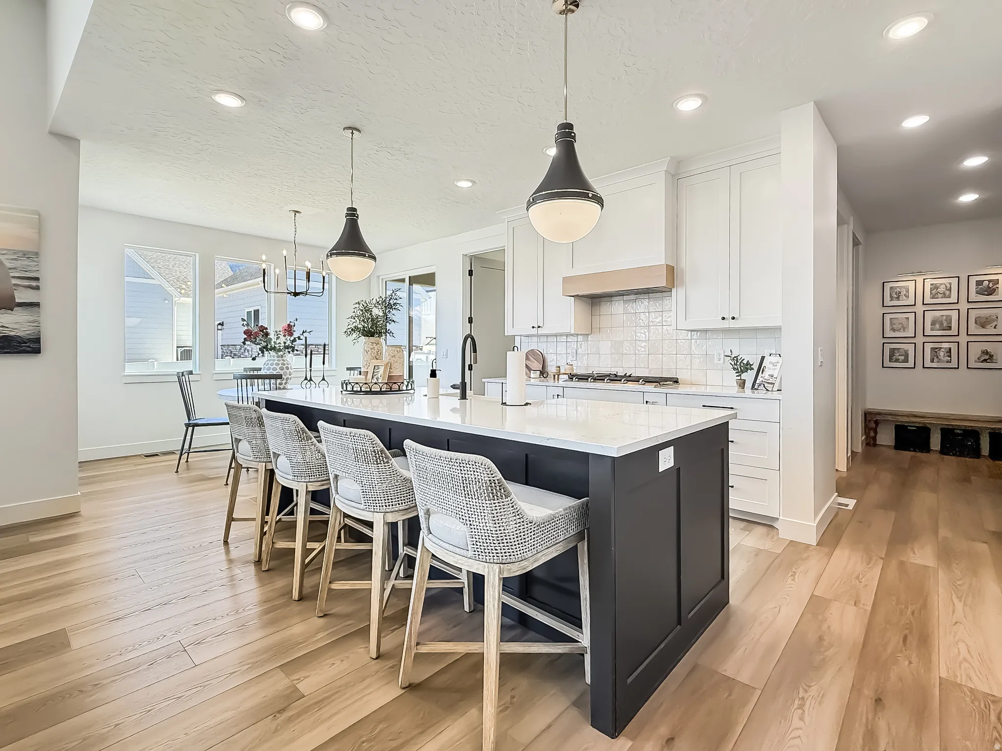 Kitchen with dual tone cabinetry, a kitchen bar, an island with sink, light wood finished floors, and hanging light fixtures