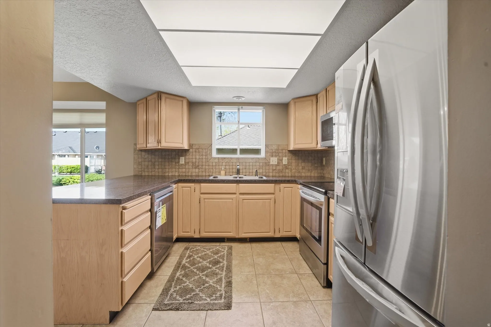 Kitchen with stainless steel appliances, a peninsula, dark countertops, wood finish cabinetry, and backsplash