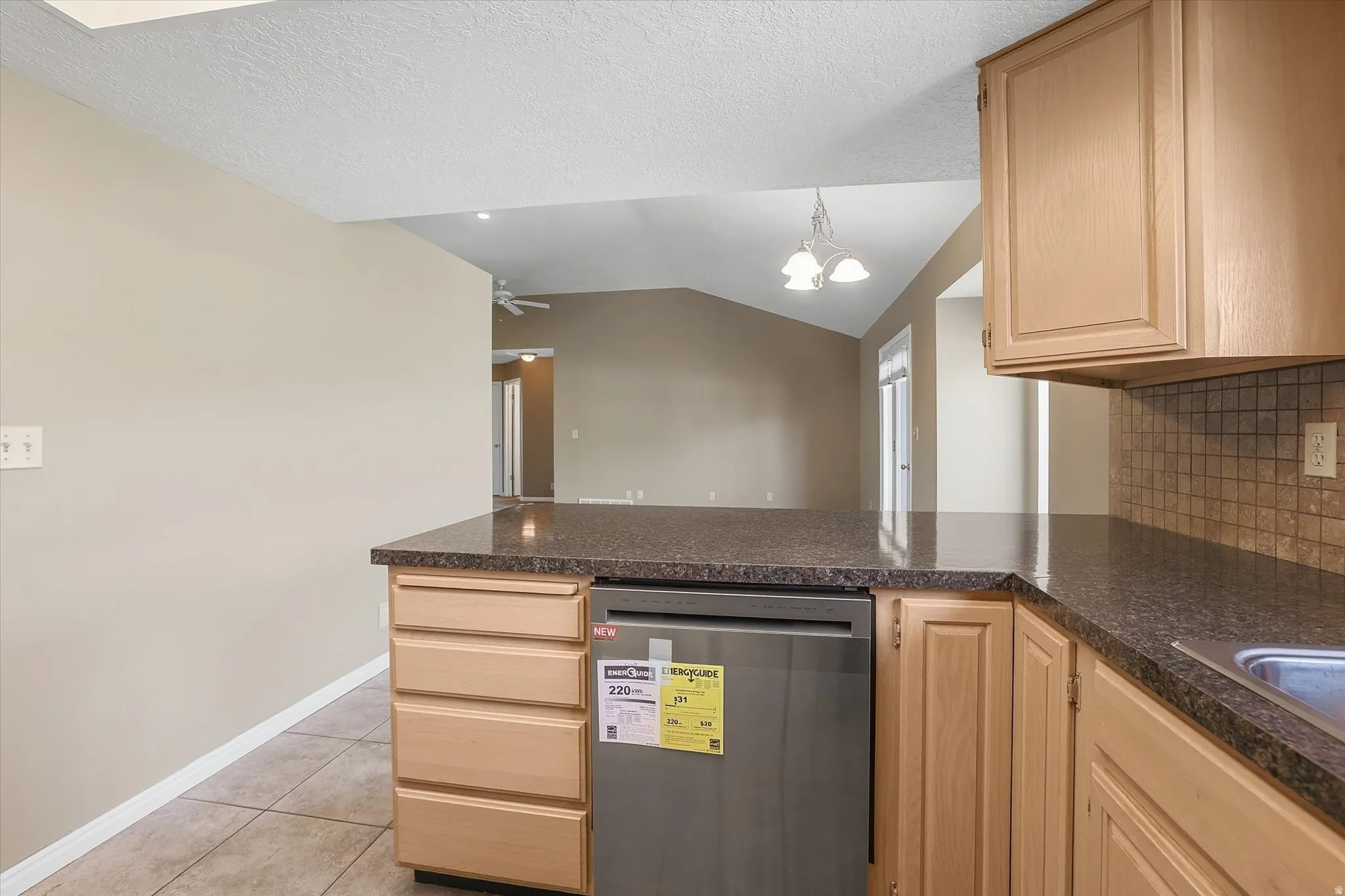 Kitchen featuring dishwasher, wood finish cabinetry, decorative backsplash, and dark countertops