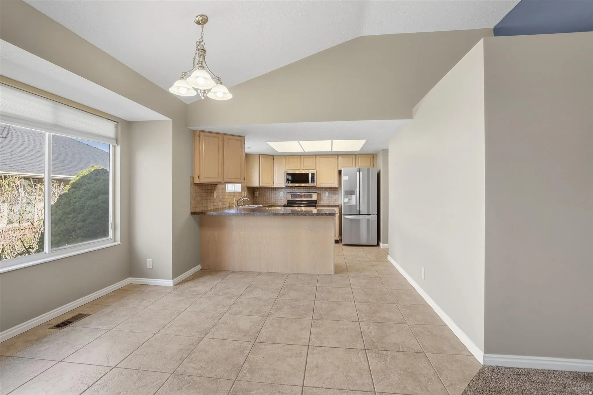 Kitchen featuring stainless steel appliances, backsplash, a peninsula, wood finish cabinets, and tiled floor