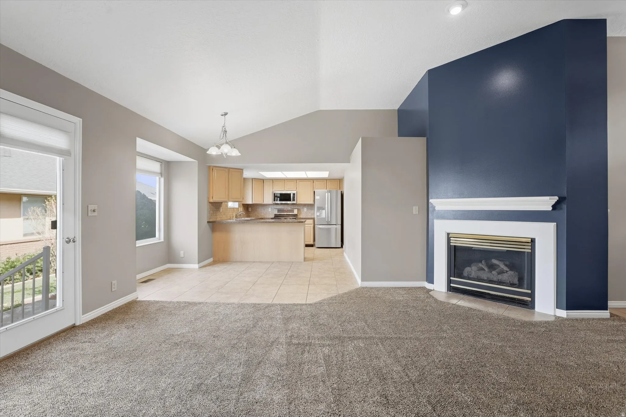 Living room with vaulted ceiling, a fireplace, and suspended lighting