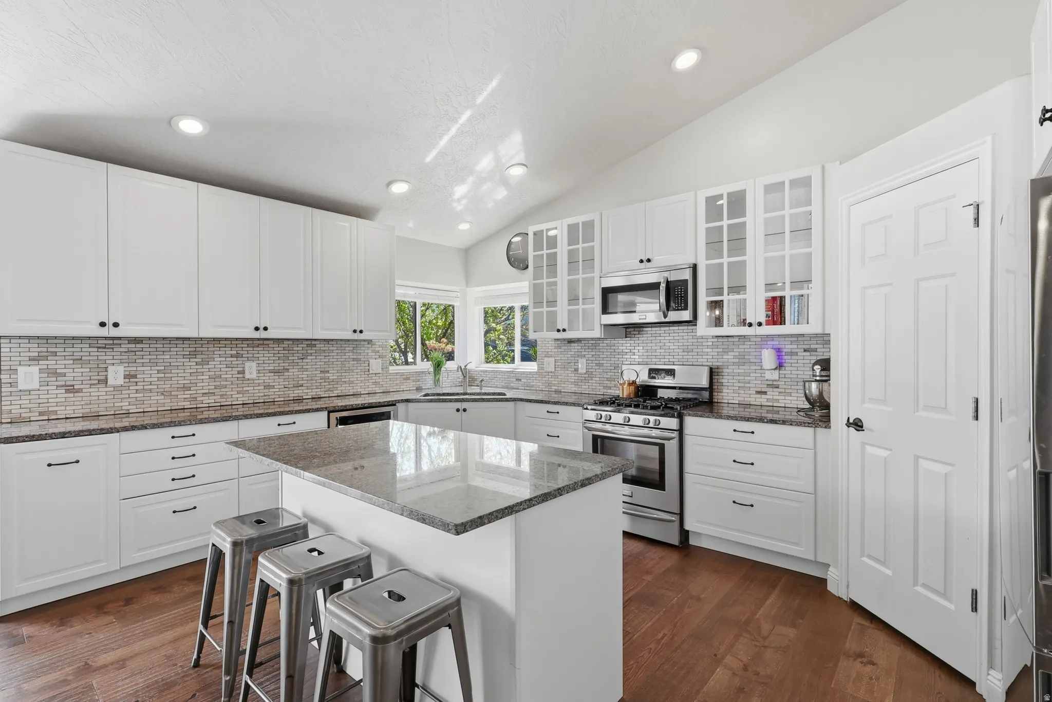 Kitchen featuring dark stone countertops, stainless steel appliances, lofted ceiling, white cabinetry, and a breakfast bar area