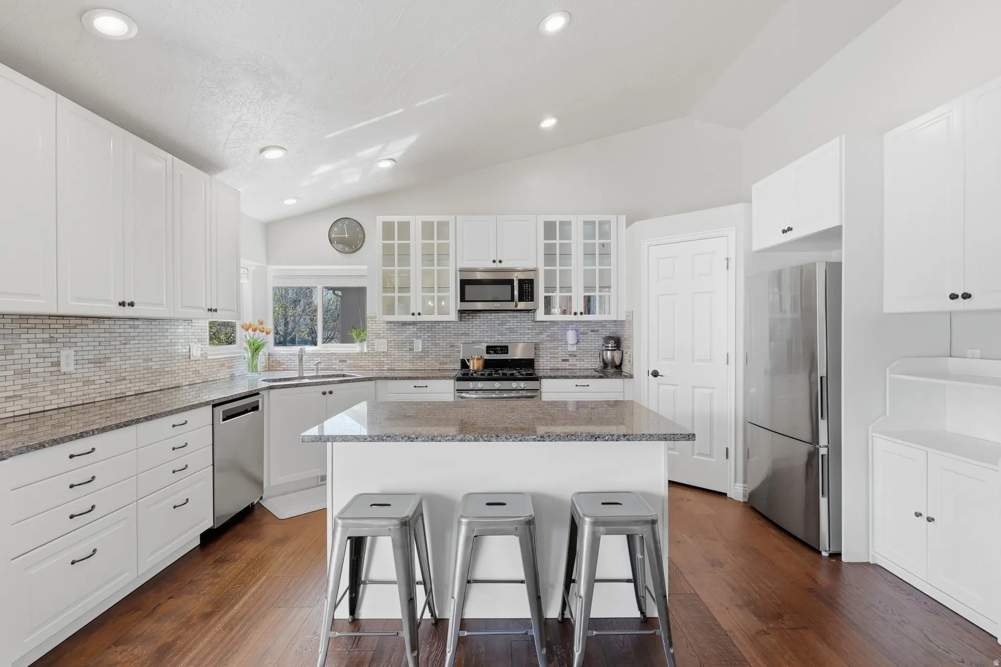 Kitchen with vaulted ceiling, stainless steel appliances, glass fronted cabinets, a center island, and recessed lighting