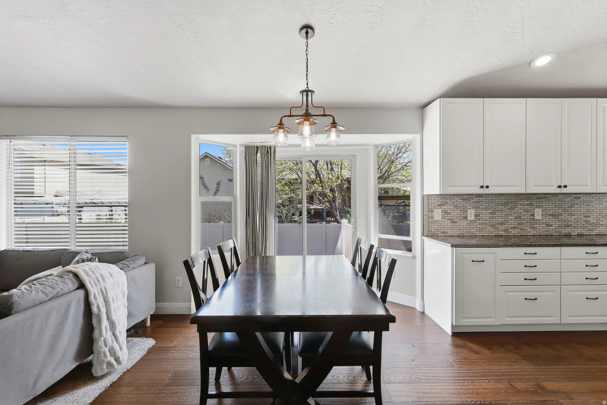 Dining room with hanging lights, wood  floors, vaulted ceiling & large windows & sliding door to the backyard