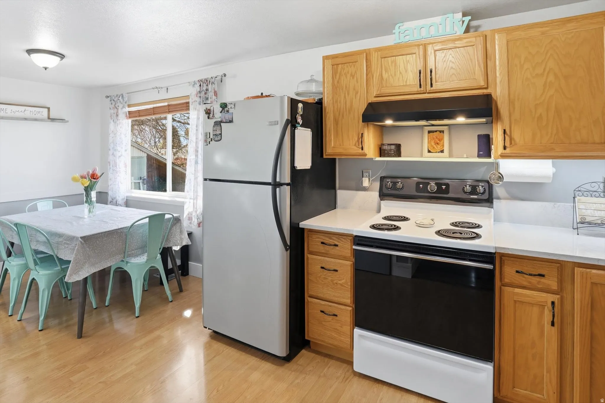 Kitchen featuring range with electric stovetop, freestanding refrigerator, light wood-type flooring, and light stone counters