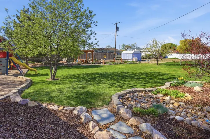 Fenced backyard featuring a storage unit and a playground