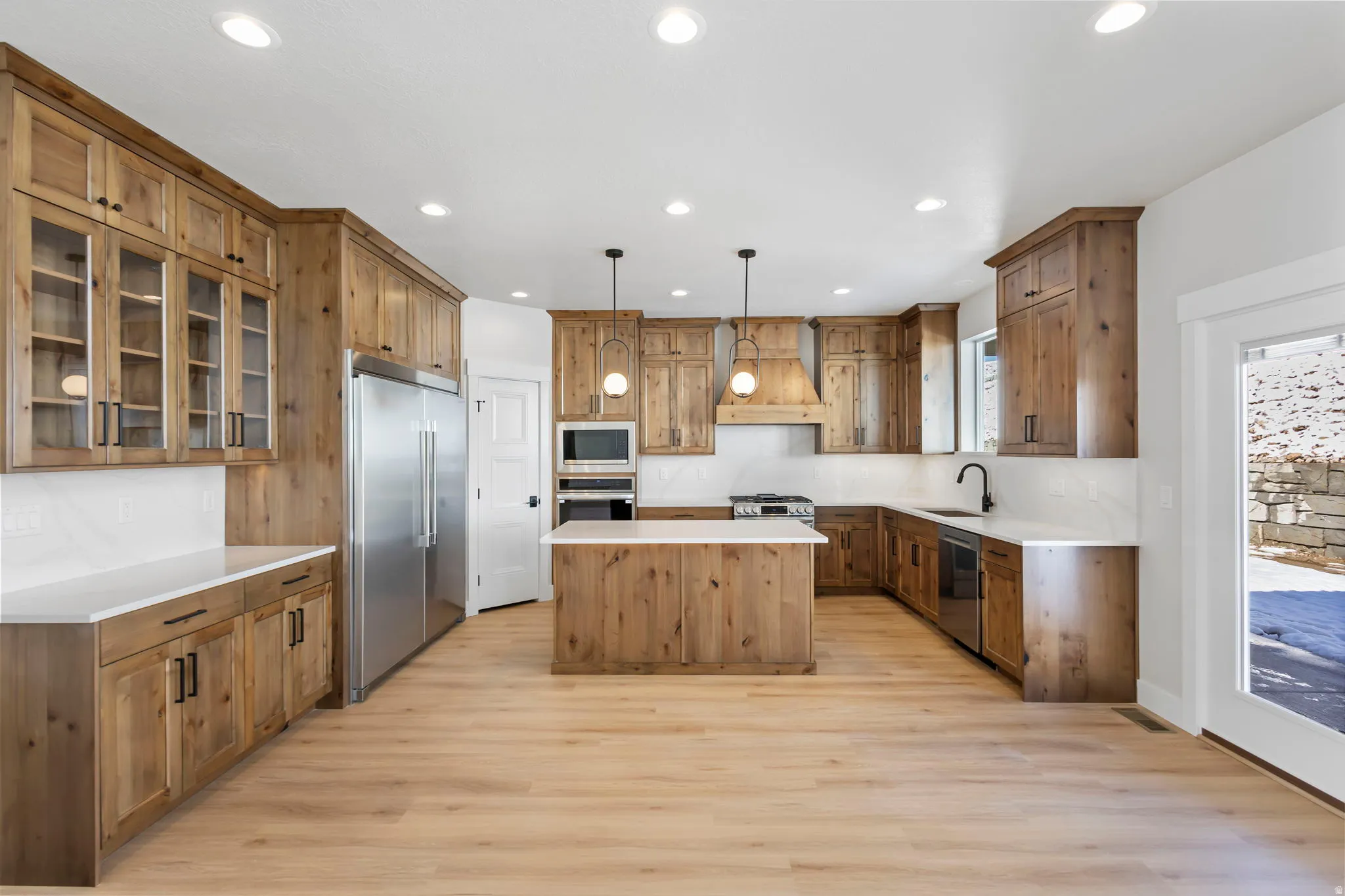 Kitchen with glass fronted cabinets, a center island, built in appliances, and light wood-style flooring