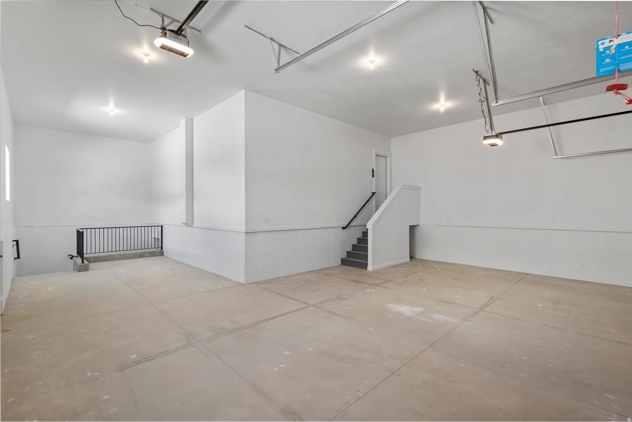 Spacious garage featuring a concrete floor, bright overhead lighting, painted walls, and an interior staircase with a handrail