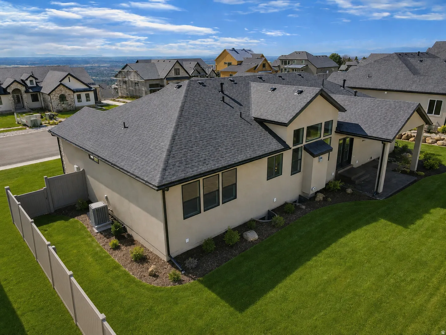 Modern stucco exterior with black-framed windows, a covered patio, dark asphalt shingle roofing, and a substantial green lawn